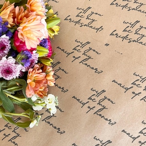 May include: Brown paper with the text "Will you be my bridesmaid?" and "Will you be my maid of honor?" repeated in a pattern. A bouquet of flowers is in the top left corner of the image.