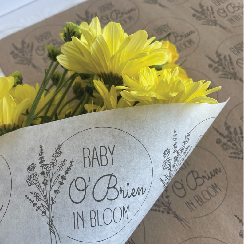 May include: A bouquet of yellow flowers wrapped in white tissue paper with a black and white sticker that says "Baby O'Brien in Bloom".