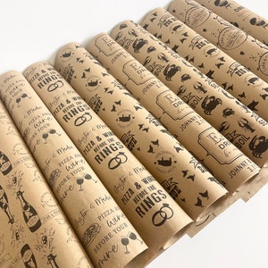 May include: A stack of brown paper gift wrap rolls with a repeating pattern of a pizza slice, wine glass, and the text "Pizza & Wine Before the Rings".