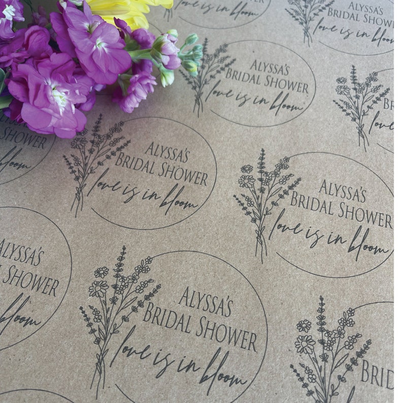 May include: Brown paper gift wrap with a repeating pattern of floral designs and the text "Alyssa's Bridal Shower Love is in Bloom".