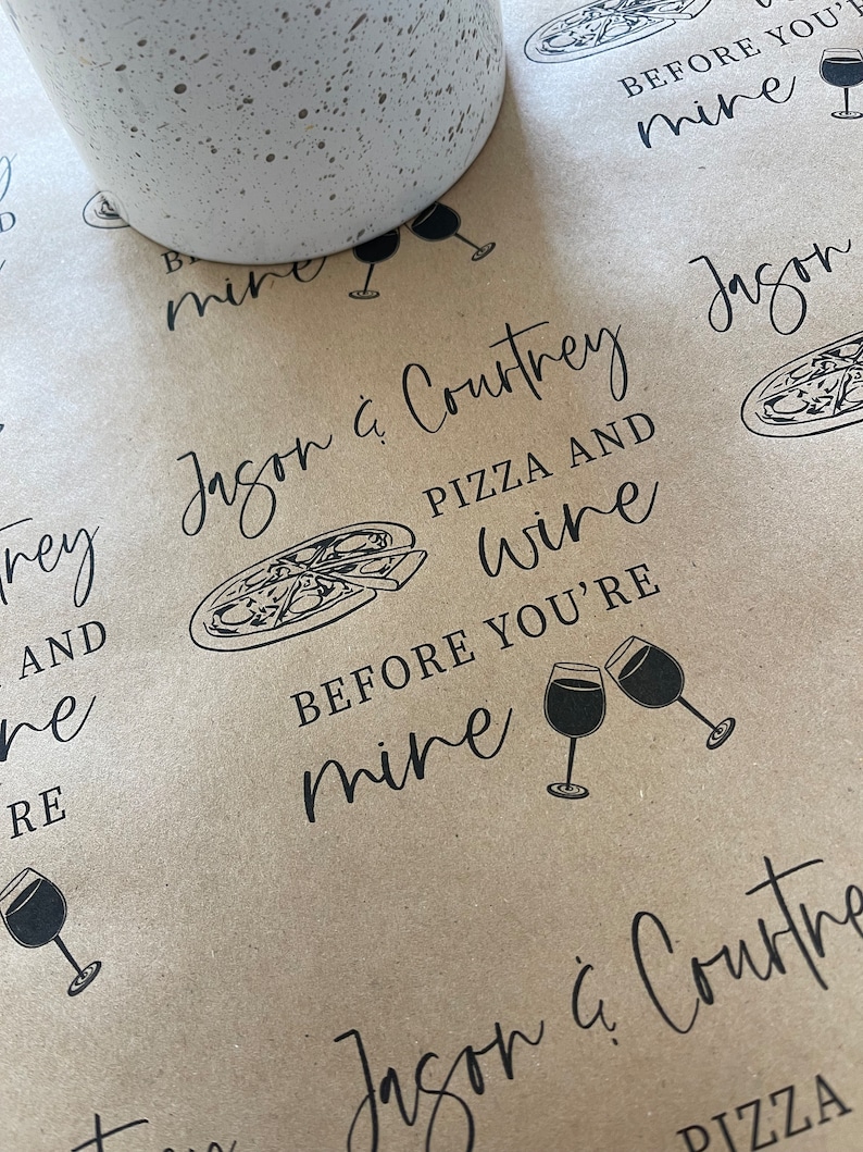 May include: Brown paper gift wrap with the text "Jason & Courtney Pizza and Wine Before You're Mine" repeated in black lettering. The design also includes a pizza slice, wine glasses, and a small potted plant.
