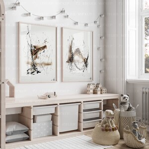 May include: A white wooden shelf unit with four open cubbies, each containing a white storage bin. The shelf is decorated with two framed abstract paintings, a string of white lights, and various toys, including a toy airplane, wooden houses, a stuffed panda bear, and a stuffed dog.