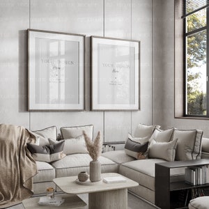 Könnte beinhalten: Zwei gerahmte Bilder mit dem Text "YOUR DESIGN Here" hängen an einer hellgrauen Wand über einem weißen Ecksofa mit Kissen und einer Decke. Das Sofa steht in einem Wohnzimmer mit einem Couchtisch, einer Vase mit Trockenblumen und einem Bücherregal.