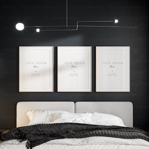 Puede incluir: Tres marcos de fotos blancos con paspartús negros colgados en una pared gris oscuro sobre una cama blanca con una manta de lana negra. Los marcos están vacíos y tienen el texto "Your Design Here" y "C2 Atelier Mockup Store" impreso en su interior.