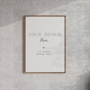 Könnte beinhalten: Ein gerahmtes Mockup mit weißem Hintergrund und dem Text "YOUR DESIGN Here" und "C2 Atelier Mockup Store". Der Rahmen ist aus hellem braunem Holz und der Hintergrund ist eine graue Betonwand.