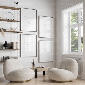 May include: Four black framed posters with white backgrounds and the text "Your Design Here" hanging on a white wall. Two white fluffy armchairs are in front of the posters, and a small wooden table with a book and a pencil holder is between the chairs. A window with a view of green trees is in the background.