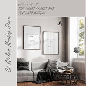 May include: A mockup of two framed posters hanging on a white wall in a living room. The posters are both black framed and have a white background with the text "YOUR DESIGN Here" in black. The posters are hanging above a gray couch with black and white throw pillows and a black throw blanket. There is a black coffee table in front of the couch with a book and a candle on it.