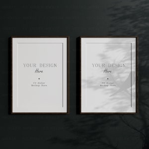 Puede incluir: Dos carteles enmarcados en negro con monturas blancas colgados en una pared gris oscuro. Los carteles tienen el texto "YOUR DESIGN Here" y "C2 Atelier Mockup Store".