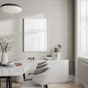 May include: A white framed poster mockup with the text "Your Design Here" and "C2 Atelier Mockup Store" in a modern dining room setting. The room features a white table with chairs, a white cabinet with vertical grooves, and a vase with dried flowers.