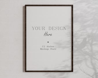 Könnte beinhalten: Ein schwarzer gerahmter Poster-Mockup mit dem Text "YOUR DESIGN Here" und "C2 Atelier Mockup Store" an einer weißen Wand mit dem Schatten eines Baumzweigs.