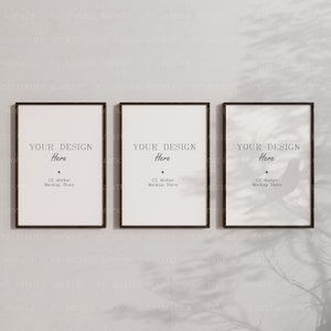 Puede incluir: Tres carteles enmarcados en negro con fondos blancos colgados en una pared gris claro. Los carteles tienen el texto "YOUR DESIGN Here" y "C2 Atelier Mockup Store" impreso en ellos.