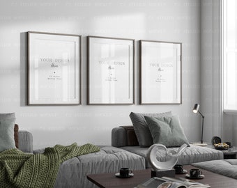 May include: Three framed pictures with white mounts and brown frames hanging on a white wall above a grey sofa with green throws and cushions. The frames are all the same size and are arranged in a row. The text in the frames reads "Your Design Here".