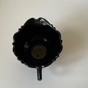 以下が含まれることがあります： 真上から見た光沢のある黒い陶器製のクリーマーピッチャー。容器には波打つようなスカラップ状の縁があり、側面にはハンドルが一つ付いています。内部は深く暗く、滑らかな表面に光が反射しています。