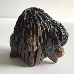 May include: A hand-carved wooden sculpture of a bison. The bison has a dark brown body and a shaggy, textured mane in shades of black and brown. The sculpture has a detailed, rustic appearance.