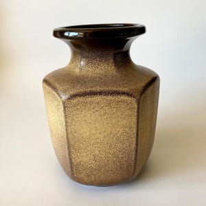 May include: A hexagonal ceramic vase featuring a gradient finish that transitions from a dark brown rim to a speckled golden-tan body. The vase has a wide, flared opening and a structured, multi-sided shape with a smooth, glossy surface texture.