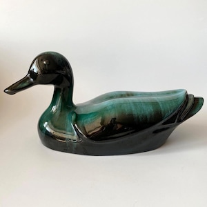 May include: A ceramic duck figurine in shades of black and teal. The duck has a glossy finish and a detailed design, with a long beak and a curved body. The figurine is a decorative item.