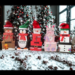 May include: A selection of Christmas-themed gift boxes, each designed to look like a different character, such as a snowman, penguin, and Santa Claus. The boxes are stacked and arranged in front of a Christmas tree.