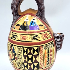 May include: A ceramic pitcher with a brown animal head spout and a geometric pattern in shades of red, yellow, black, and white. The pitcher has a small handle and a round base.