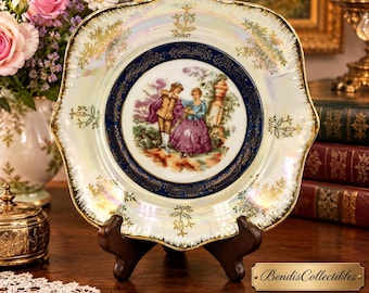 May include: A square 7-inch lusterware plate featuring a central illustration of a couple in period clothing. The plate has a scalloped edge, a deep blue border with gold filigree, and a pearlescent finish with gold floral accents throughout.