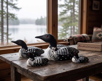 May include: A set of four hand-painted wooden loon figurines in varying sizes, featuring black bodies with white spotted and striped patterns, red eyes, and pointed beaks. A small wooden block with the text BendisCollectibles is present.