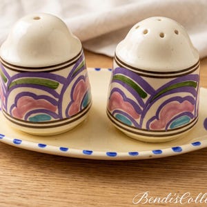 May include: A ceramic salt and pepper shaker set on an oval tray, featuring a cream base with hand-painted scalloped patterns in purple, pink, and teal, accented by dark brown lines and a blue dotted rim on the tray, with Bendi'sCollectibles text.