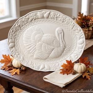 May include: An oval-shaped cream-colored ceramic serving platter featuring a raised relief of a turkey in the center. The border is decorated with embossed fruits, flowers, and a lattice pattern. The platter has a smooth, matte finish.