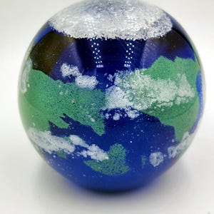 May include: A blue glass globe with white and green swirls. The globe is a decorative piece and has a white cloudy top.