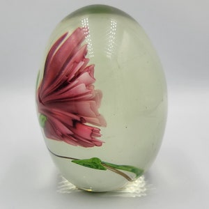 May include: A clear glass paperweight with a pink flower inside. The flower has green leaves and a stem.