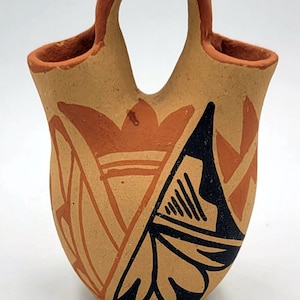 Może przedstawiać: Mały, ręcznie malowany wazon ceramiczny z uchwytem. Wazon jest ozdobiony geometrycznymi wzorami w kolorze czarnym, pomarańczowym i brązowym.