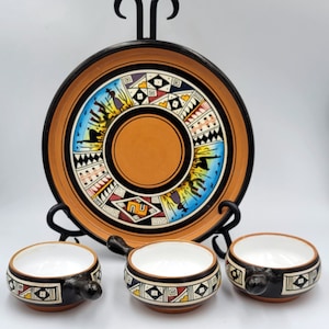 May include: A set of four ceramic bowls with a black and white geometric design. The bowls are arranged on a larger plate with a similar design. The plate is on a black metal stand.