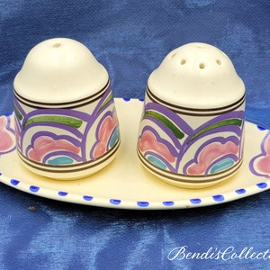 May include: A set of two white ceramic salt and pepper shakers with a floral design in shades of pink, purple, green, and blue. The shakers are on a white oval tray with a blue dotted border.