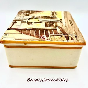 May include: A rectangular ceramic trinket box with a cream-colored base and a lid featuring a sepia-toned illustration of a building facade. The lid and base are trimmed with a thin, brown border. The text "BendisCollectibles" is at the bottom.