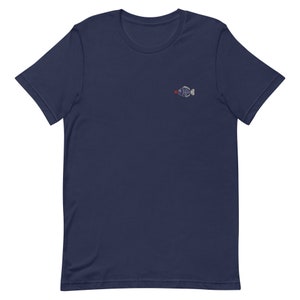May include: A navy blue t-shirt with a small embroidered fish design. The fish is white with a red mouth and black eyes.