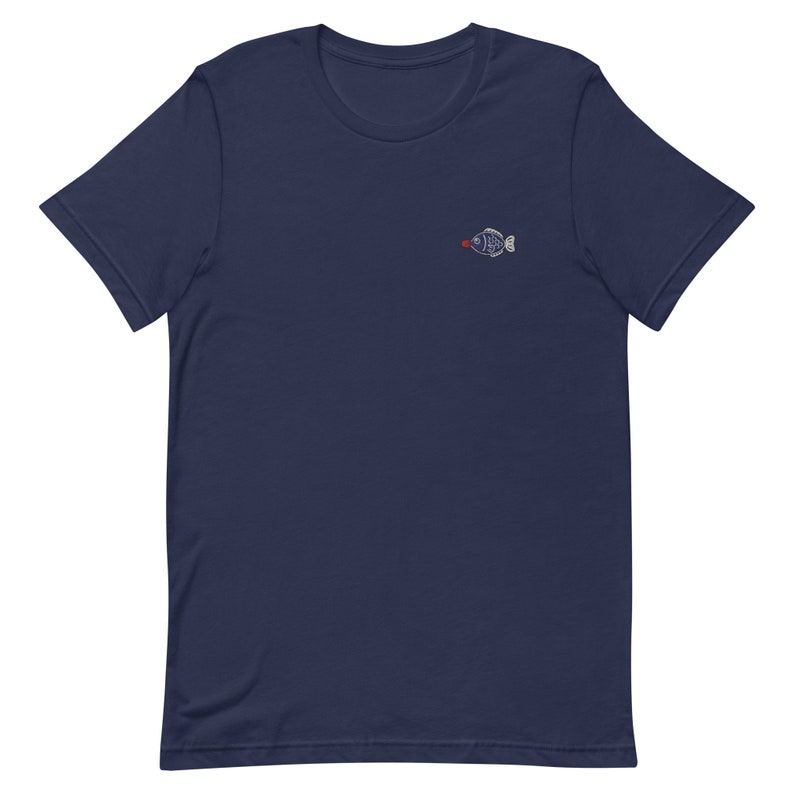 May include: A navy blue t-shirt with a small embroidered fish design. The fish is white with a red mouth and black eyes.