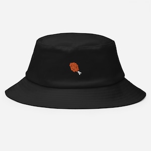 Pode incluir: Chapéu de pescador preto com uma pequena imagem bordada de uma perna de frango frita.