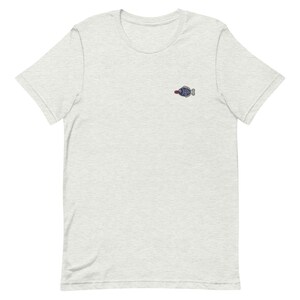 May include: A heather grey t-shirt with a small embroidered fish design in blue and red.