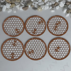 Könnte beinhalten: Sechs braune Untersetzer aus Holz mit einem Wabenmuster und Bienensilhouetten. Die Untersetzer sind in zwei Reihen mit jeweils drei Stück angeordnet.