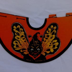 May include: A vintage orange and black butterfly-themed cutout. The cutout features a smiling face with antennae and butterfly wings with yellow and black patterns. The edges are outlined in black.