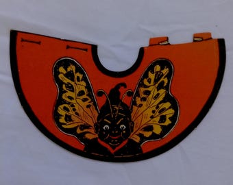 May include: A vintage orange and black butterfly-themed cutout. The cutout features a smiling face with antennae and butterfly wings with yellow and black patterns. The edges are outlined in black.