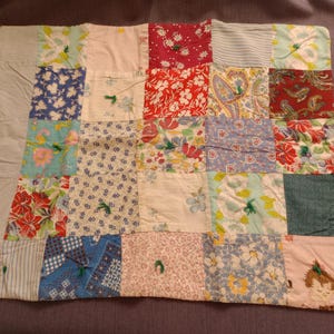 May include: A rectangular patchwork quilt featuring a variety of fabric squares with diverse patterns including floral, paisley, striped, and solid prints in red, blue, green, yellow, and white. The quilt is tied with small green yarn knots.