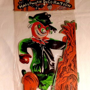 May include: Vintage Halloween decoration featuring a scarecrow with a red face, green and black clothing, and a pumpkin. The decoration is in a plastic bag with the words "Halloween Decoration" at the top, along with illustrations of a cat, bat, and skeleton.