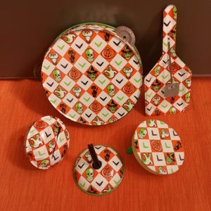 May include: A collection of Halloween-themed toys, including a tambourine, a guitar-shaped item, and several spinning tops. The toys feature a repeating pattern of skulls, pumpkins, and ghosts on a white and orange checkered background.