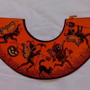 May include: Orange Halloween decoration with black silhouettes of fairies, a black cat, and jack-o'-lanterns. The decoration has a curved shape with a black border and is set against a white background.