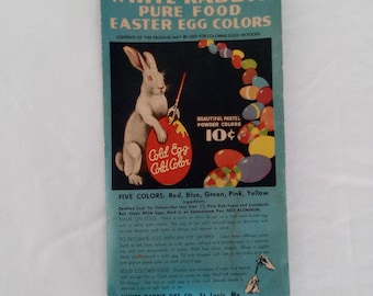 Könnte beinhalten: Vintage White Rabbit Ostereierfarben-Packung. Das Paket zeigt ein weißes Kaninchen, das ein rotes Ei bemalt. Die Packung enthält Anweisungen zum Färben von Eiern in fünf Farben.