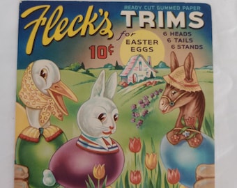May include: Vintage Fleck's Easter Trims package. The package features illustrations of a duck, a rabbit, and a donkey, each emerging from an egg. The text reads "Ready Cut Gummed Paper Trims for Easter Eggs". The package is marked "10¢" and includes the text "6 Heads, 6 Tails, 6 Stands".