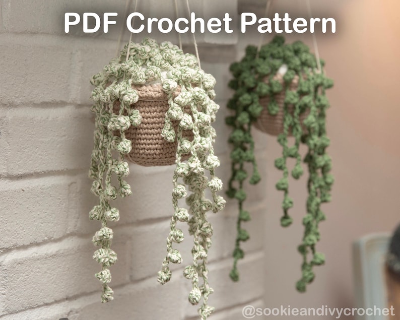 May include: Two crocheted hanging plants, one in a beige pot with light green leaves and the other in a brown pot with dark green leaves. The plants are hanging from a white brick wall. The text "PDF Crochet Pattern" is at the top of the image. The text "@sookieandivycrochet" is at the bottom of the image.