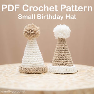 Puede incluir: Dos gorros de cumpleaños de ganchillo con pompones. Un gorro es blanco con un pompón beige y un borde beige. El otro gorro es beige con un pompón blanco y un borde blanco.  PDF Crochet Pattern Small Birthday Hat @sookieandivycrochet