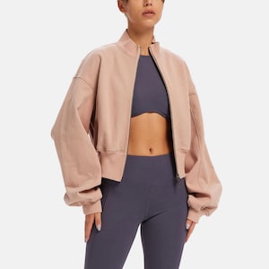 May include: A cropped blush pink zip-up bomber jacket with long sleeves and a relaxed fit.