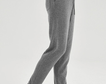 May include: Gray knit sweatpants with a drawstring waist and a single back pocket. The pants have a relaxed fit and are shown with a white top and cream-colored slip-on shoes. The pants have a split hem at the ankle.