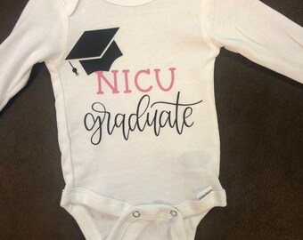Può includere: Body bianco a maniche lunghe per neonato con un cappello di laurea nero e il testo "NICU graduate" in lettere rosa.